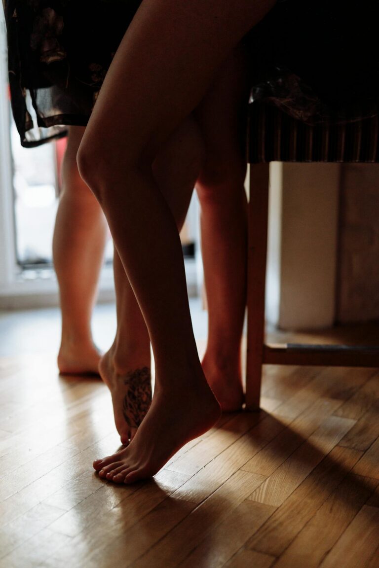 A close-up of women's bare legs and feet intertwined indoors, conveying intimacy.