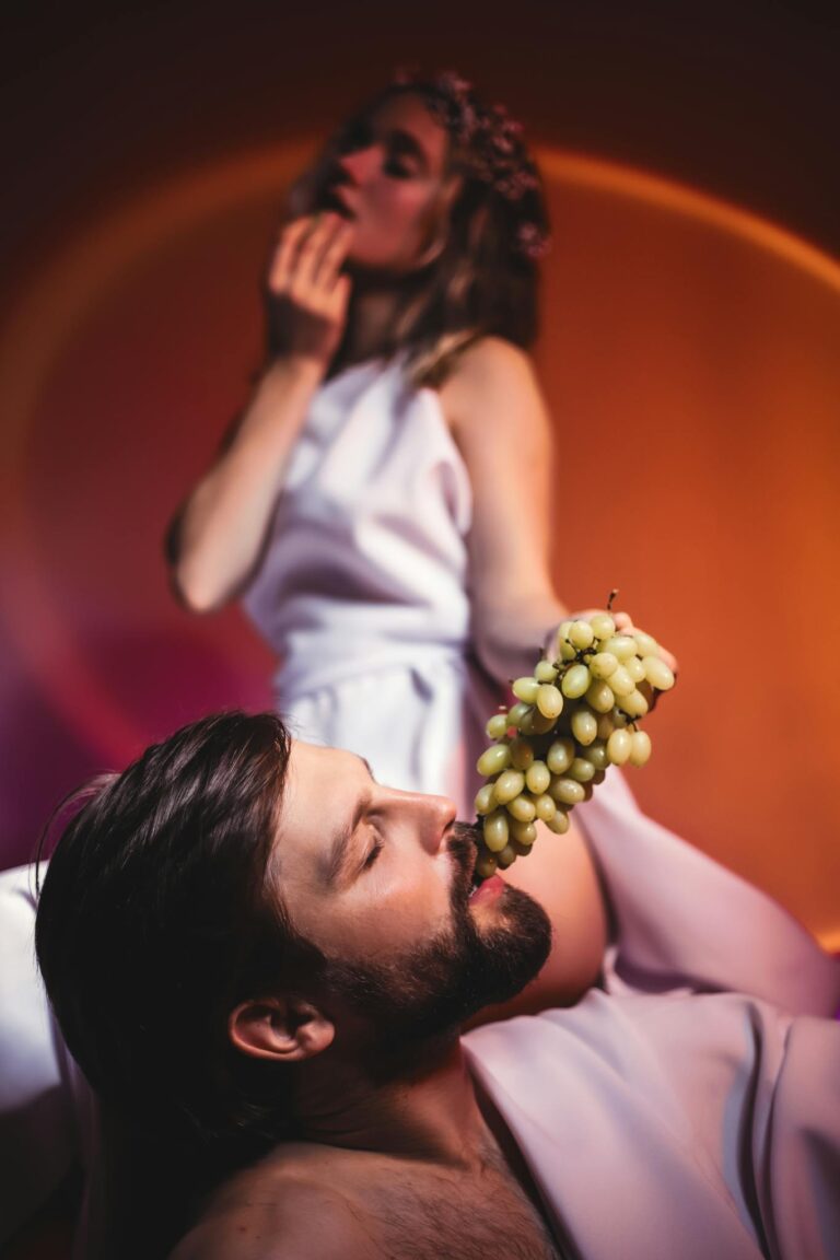 Artistic photo of two people in togas with grapes, evoking classical themes.